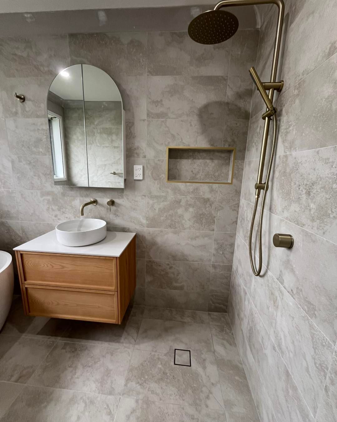 Modern Bathroom With Gray Tile, Wooden Vanity, Round Sink, Arched Mirror, and Gold Shower Fixtures — Cobra Plumbing & Bathrooms in Kiama, NSW
