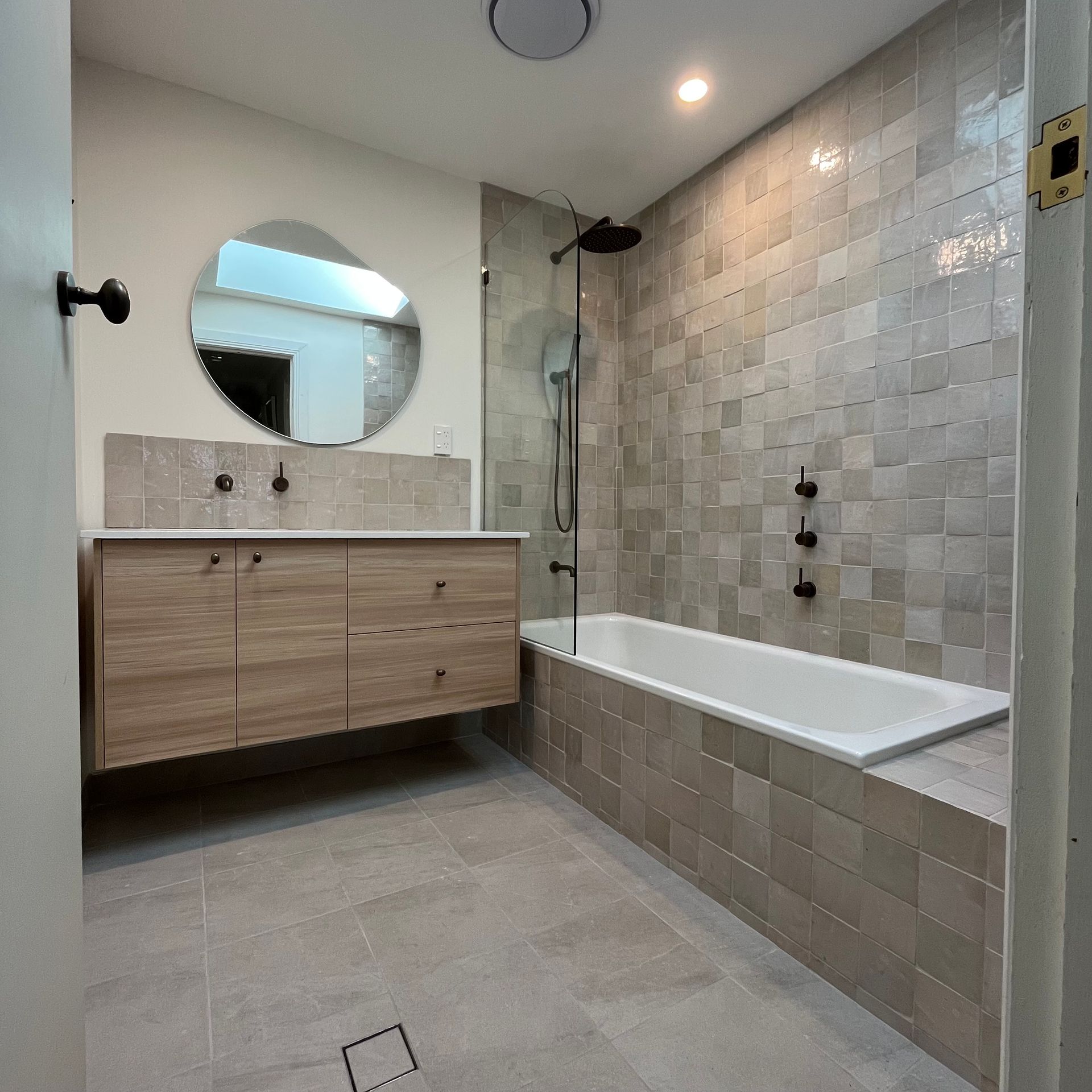 Modern bathroom with a wooden vanity, gray tiles, and a bathtub — Cobra Plumbing & Bathrooms in Heathcote, NSW