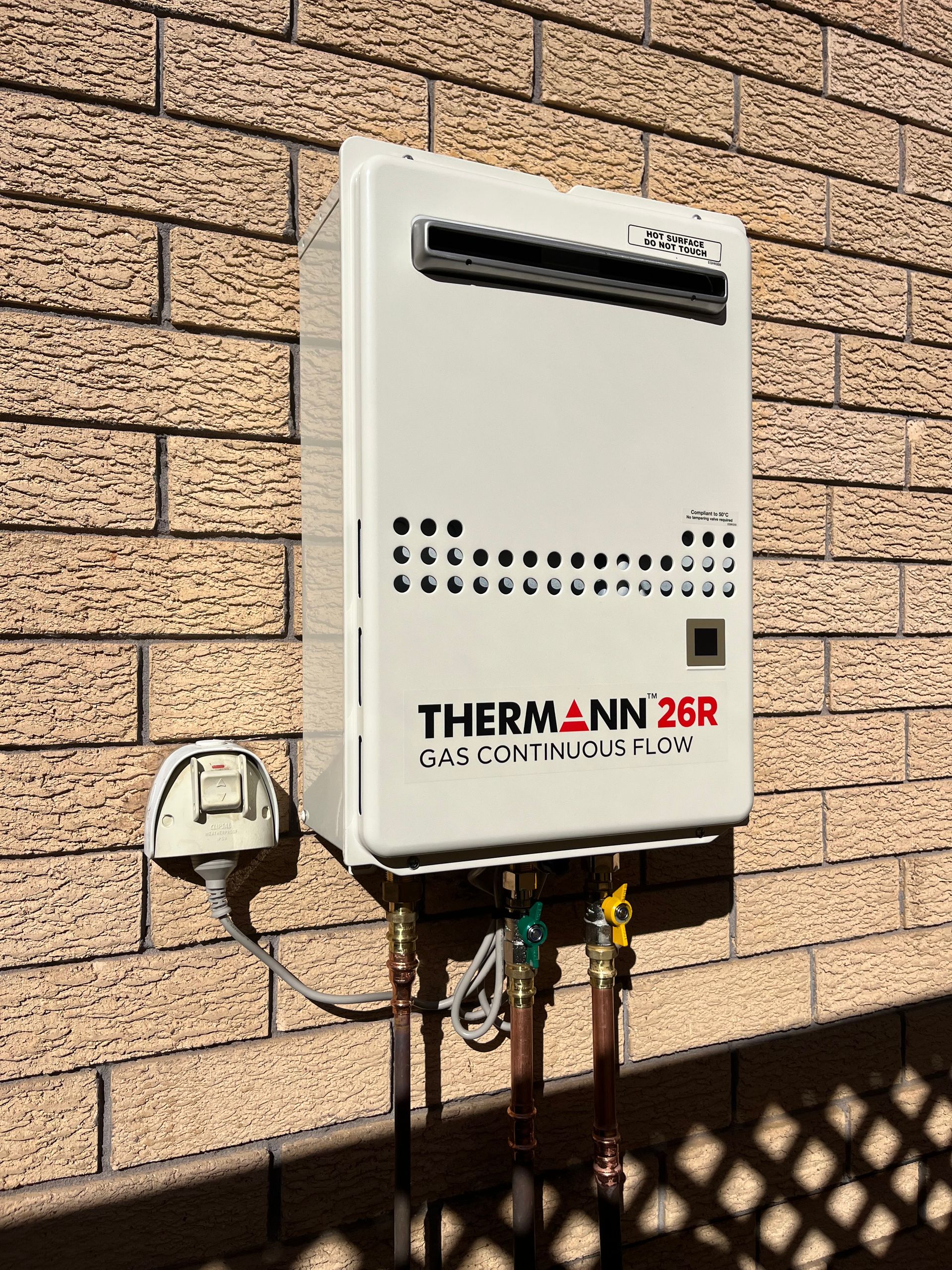 White Thermann 26R gas continuous flow water heater mounted on a brick wall — Cobra Plumbing & Bathrooms in Kiama, NSW