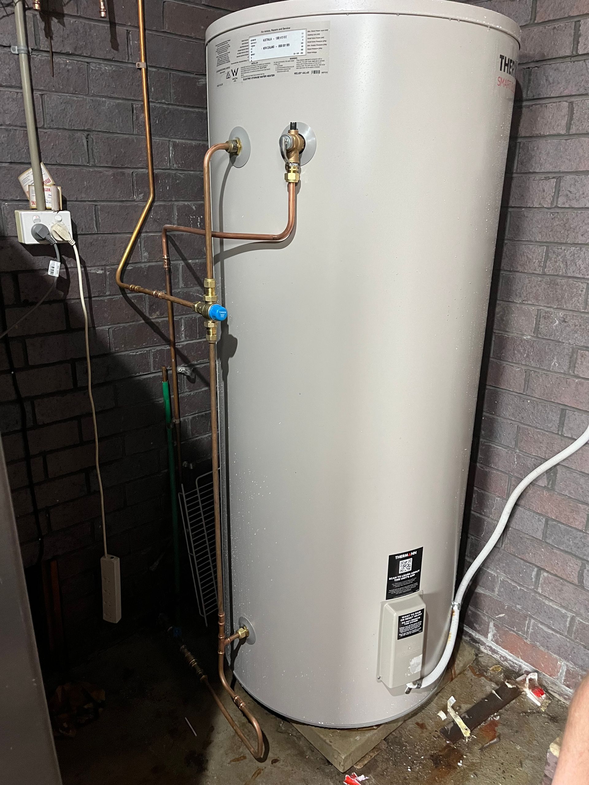 Hot water tank with copper piping in a brick-walled basement — Cobra Plumbing & Bathrooms in Heathcote, NSW