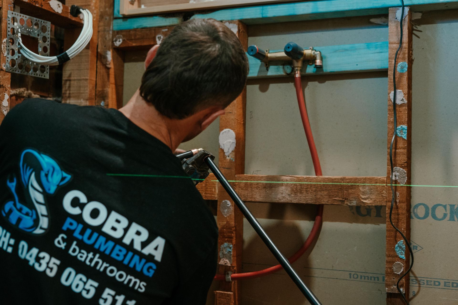 Plumber working on exposed wall pipes with tools in a bathroom or utility space — Cobra Plumbing & Bathrooms in Heathcote, NSW