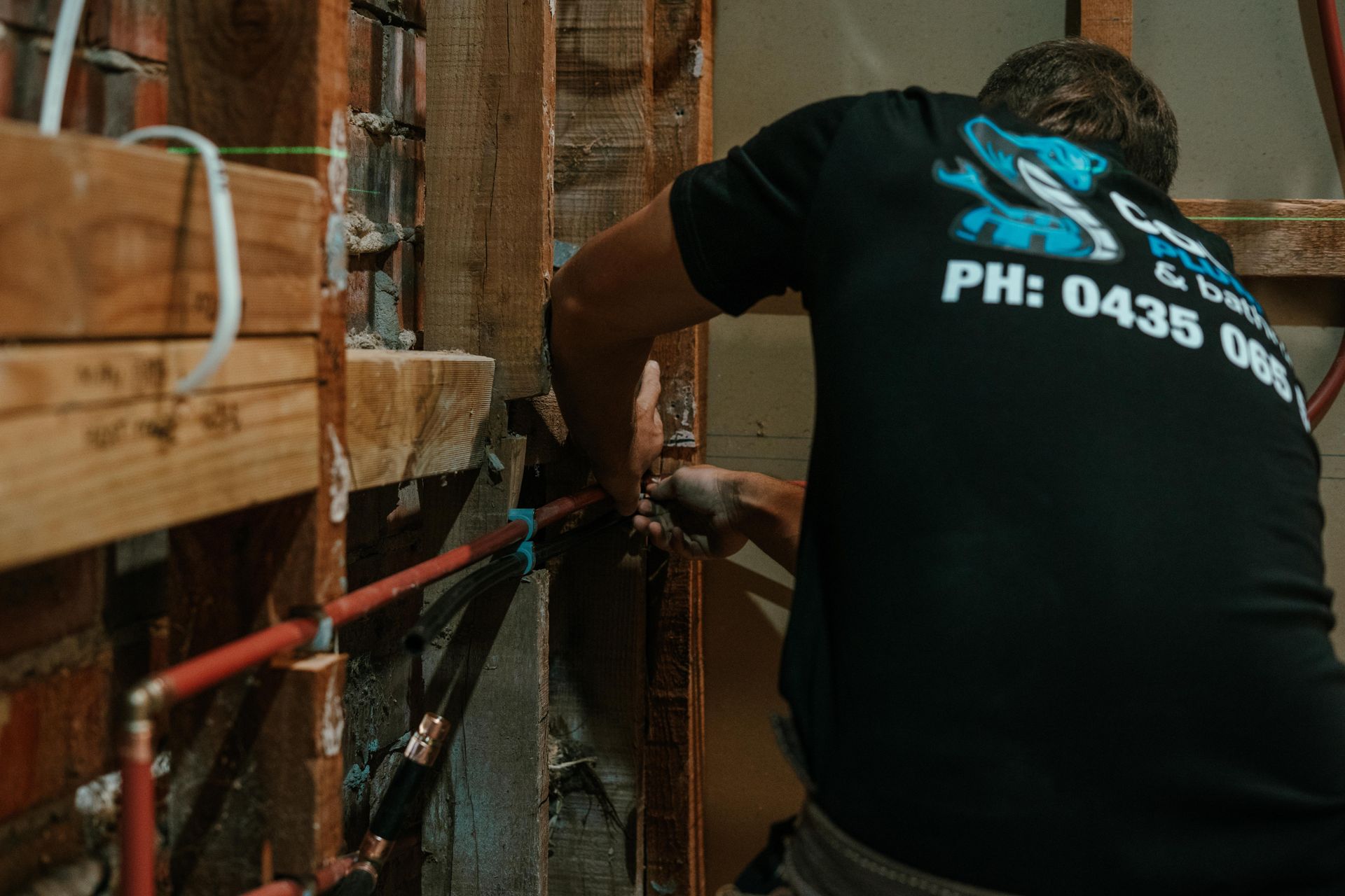 Worker using a rope harness inside a wooden structure, with red rails and a black shirt visible — Cobra Plumbing & Bathrooms in Heathcote, NSW
