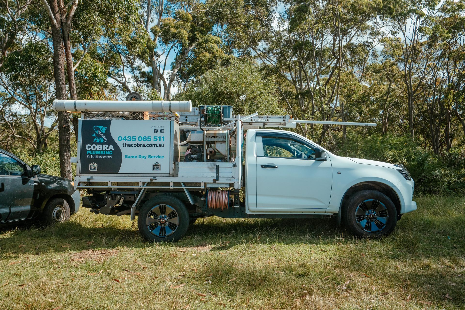 White utility pickup truck with mounted equipment parked on grass near trees — Cobra Plumbing & Bathrooms in Heathcote, NSW
