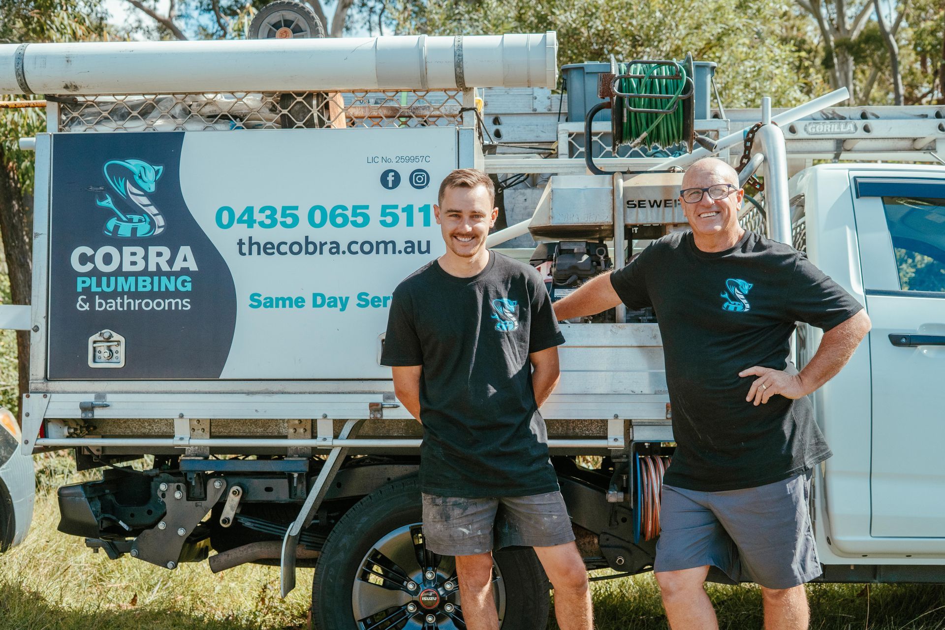 Two plumbing workers standing in front of a Cobra Plumbing service truck and equipment trailer — Cobra Plumbing & Bathrooms in Heathcote, NSW