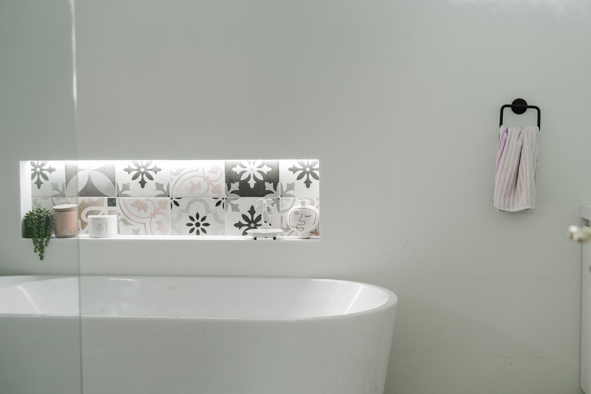 Modern bathroom with white tub, decorative tile strip, and towel on a wall hook — Cobra Plumbing & Bathrooms in Kiama, NSW