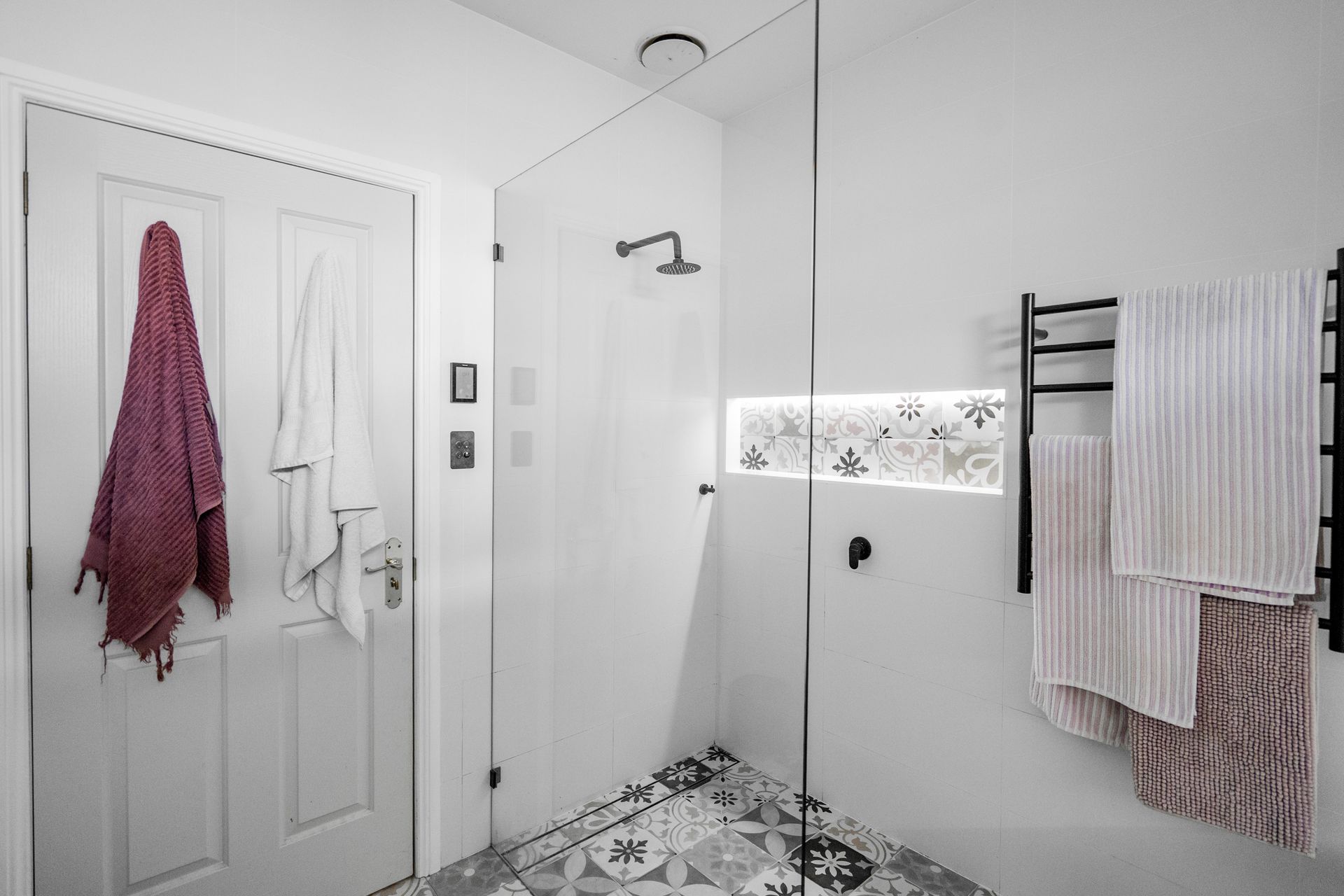 Bright white bathroom with shower, towel racks, and patterned floor tiles — Cobra Plumbing & Bathrooms in Heathcote, NSW