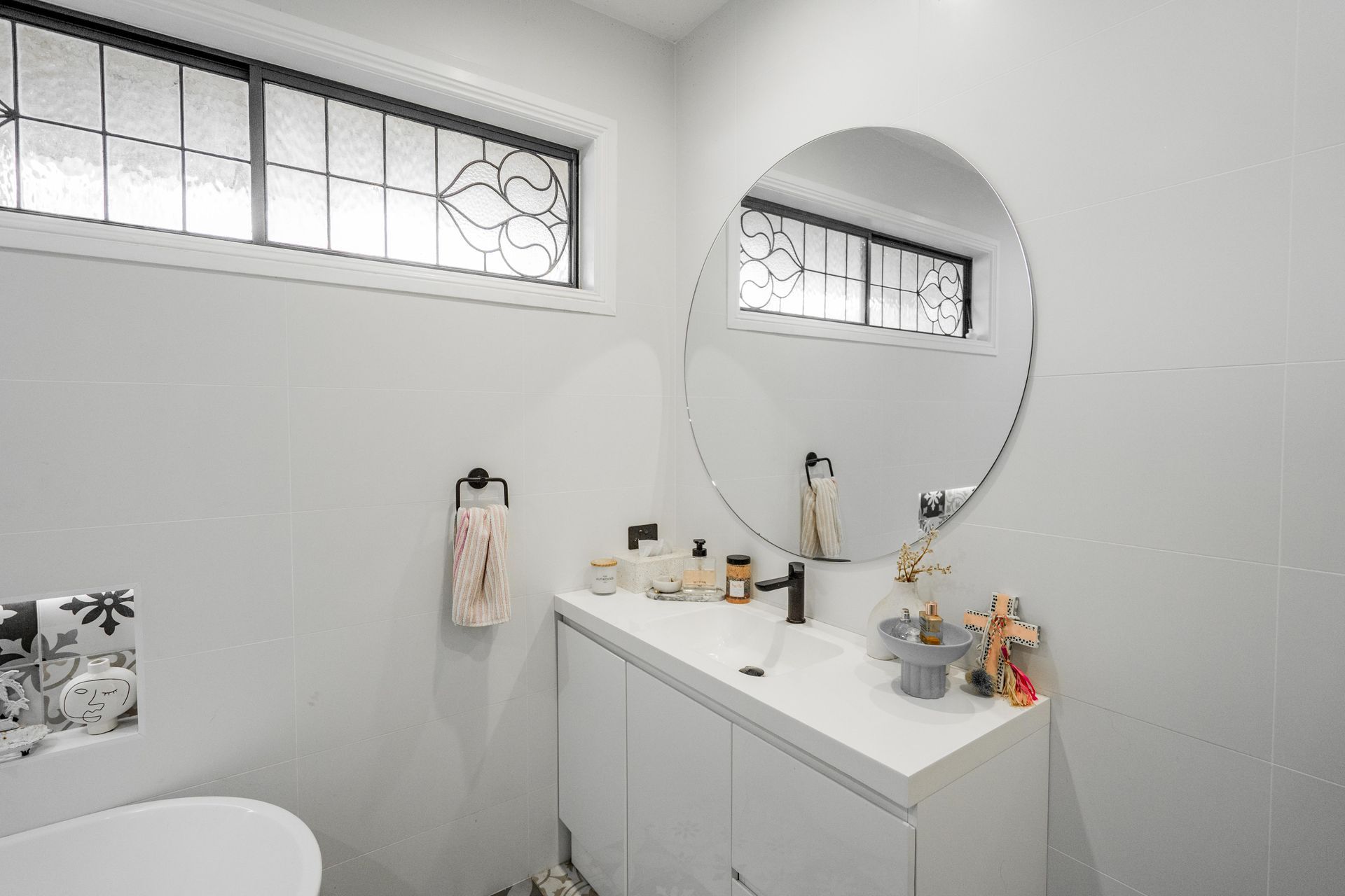 Bright white bathroom with tiled walls, oval mirror, vanity, and small high windows — Cobra Plumbing & Bathrooms in Kiama, NSW