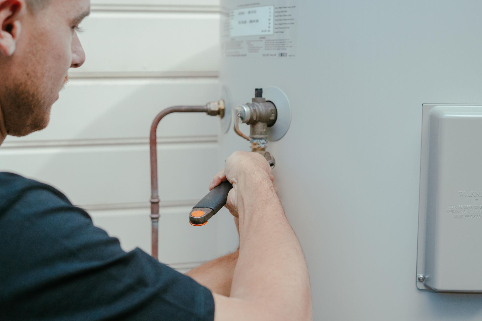 Technician using a wrench to adjust a valve on a white water heater or boiler unit — Cobra Plumbing & Bathrooms in Heathcote, NSW