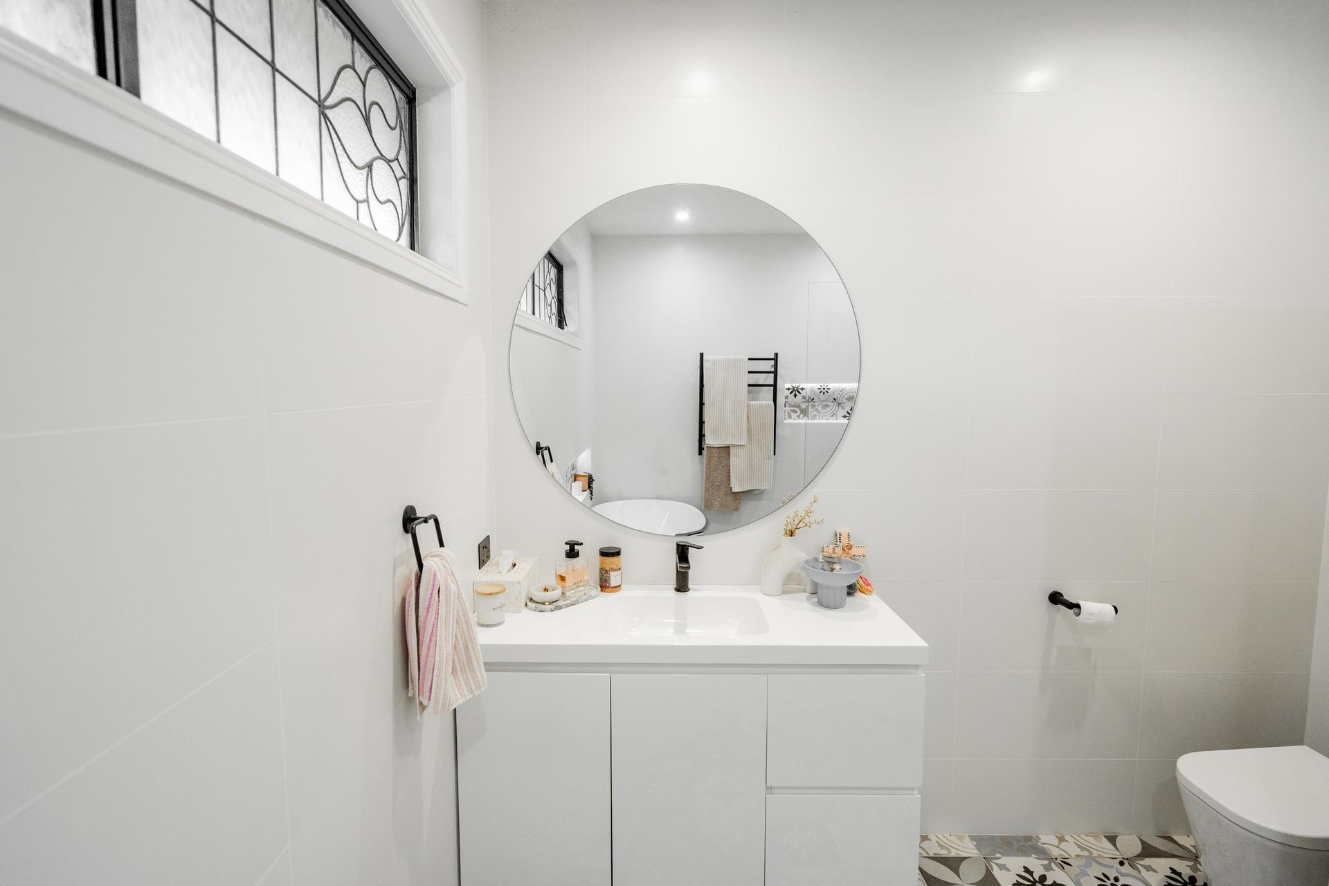 Bright white bathroom with vanity, round mirror, small window, and toilet on the right — Cobra Plumbing & Bathrooms in Heathcote, NSW