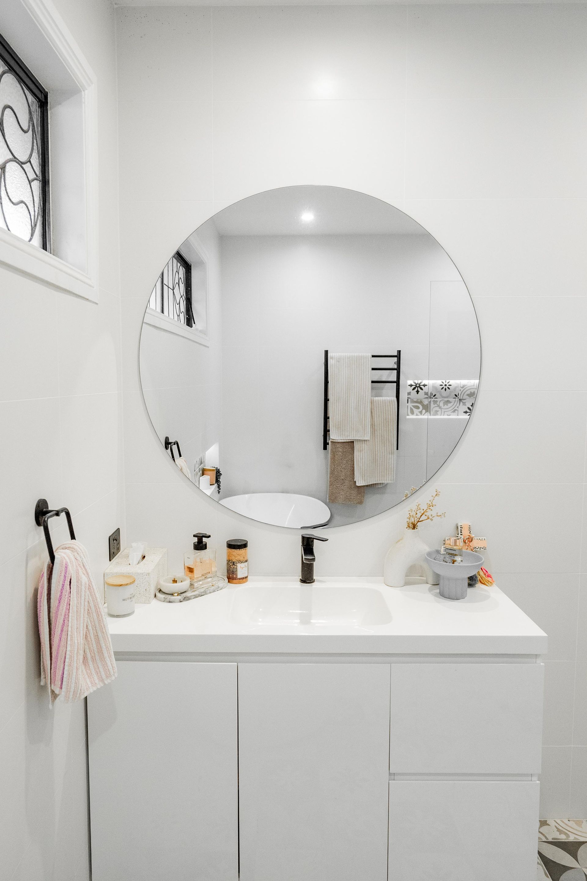 Minimal white bathroom vanity with round mirror, sink, and towels — Cobra Plumbing & Bathrooms in Kiama, NSW