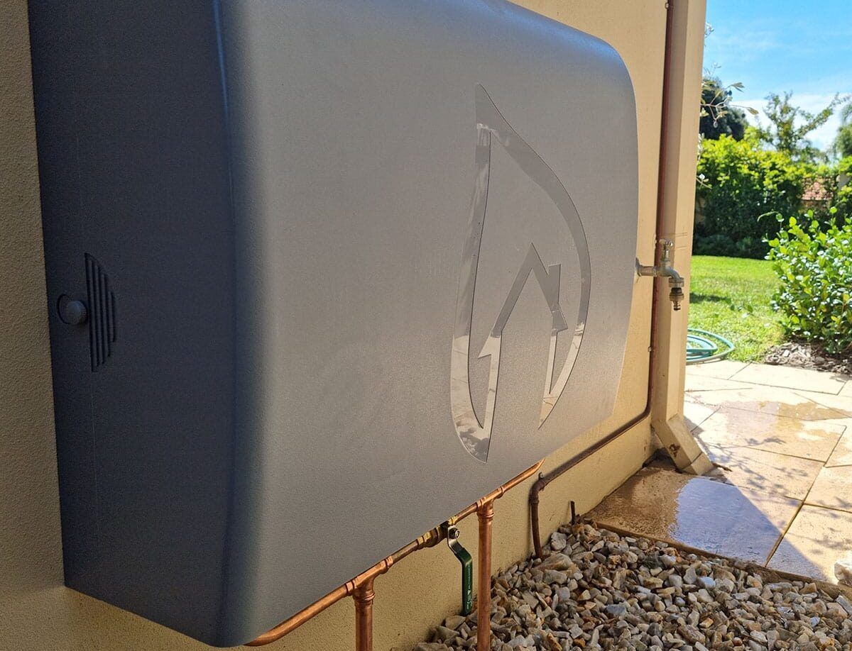 A dark gray water heater on an outdoor wall, next to a water spigot and copper pipes — Cobra Plumbing & Bathrooms in Dapto, NSW