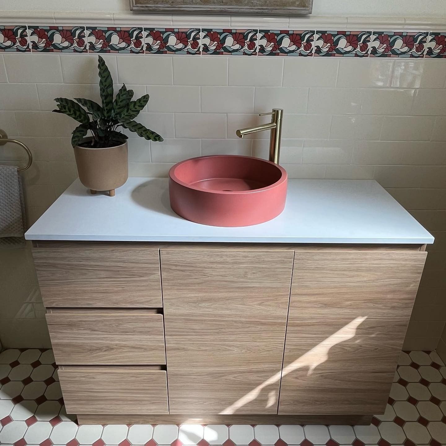 Bathroom Vanity With a Coral-coloured Sink, Gold Faucet, and Wooden Cabinets. a Plant Sits on the Counter — Cobra Plumbing & Bathrooms in Kiama, NSW