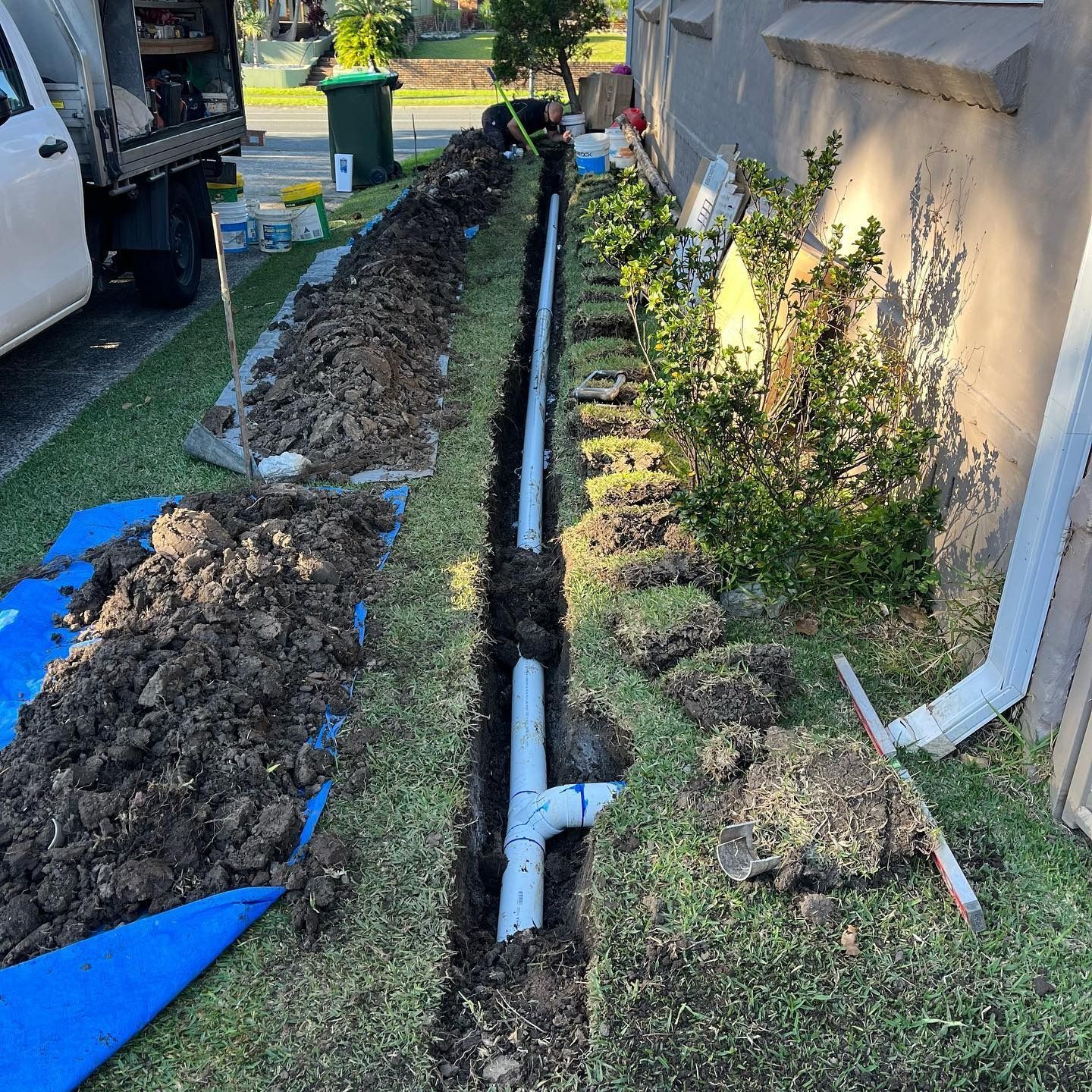 A Trench Dug in a Lawn With PVC Pipes Installed, Along the Side of a Building — Cobra Plumbing & Bathrooms in Kiama, NSW