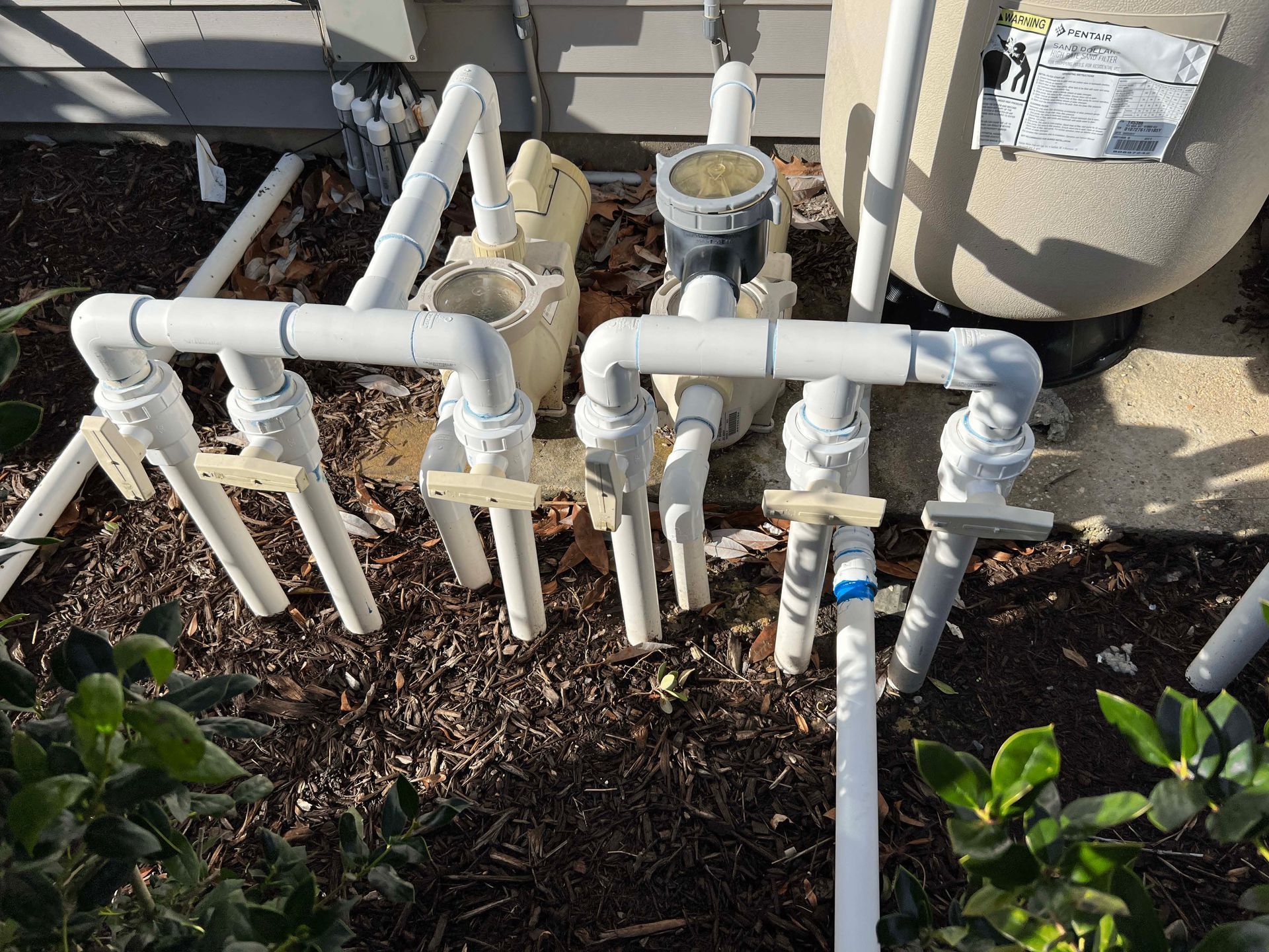 A bunch of white pipes are sitting on the ground next to a house.