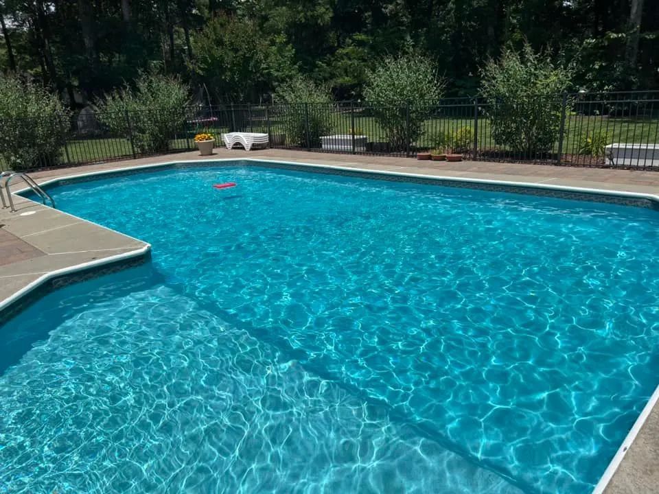 A large swimming pool with a fence around it and trees in the background.