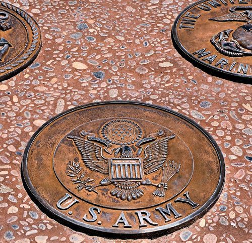 Three bronze-colored military service seals embedded in a textured concrete ground, including the U.S. Army emblem.