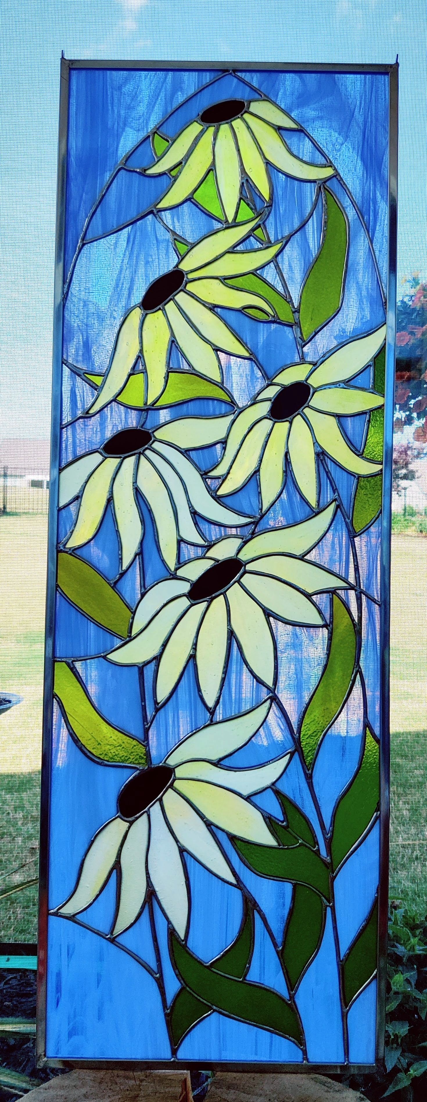 Blue stained-glass panel with white and yellow flowers and green leaves on a textured background