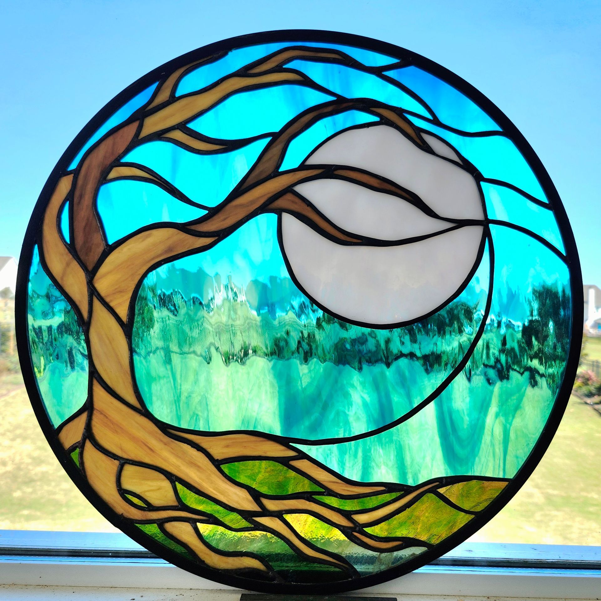 Stained-glass style circular tree with blue sky, white moon, and green forest landscape inside.