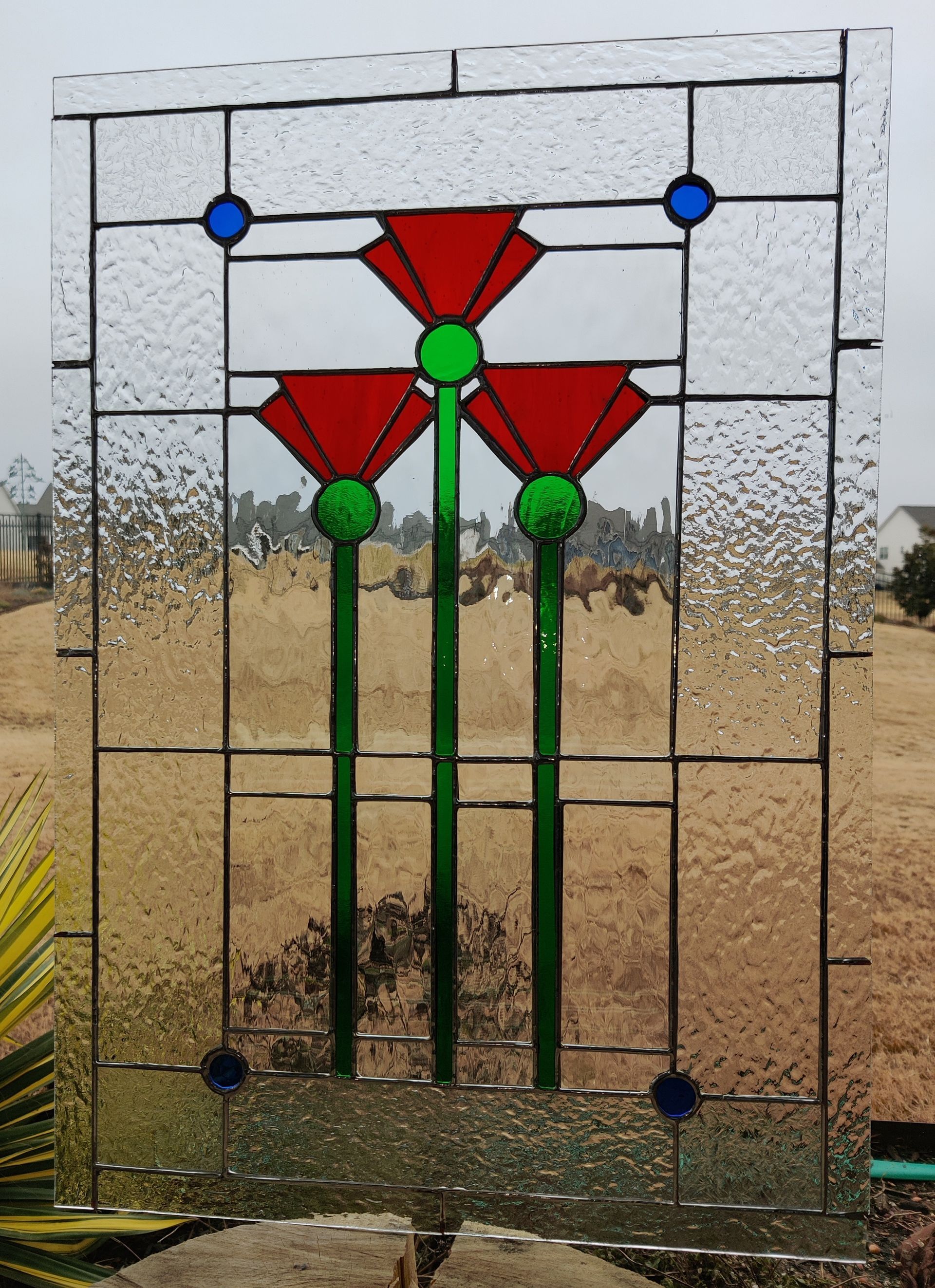 Stained-glass-style red flowers with green stems in a rectangular metal frame outdoors.