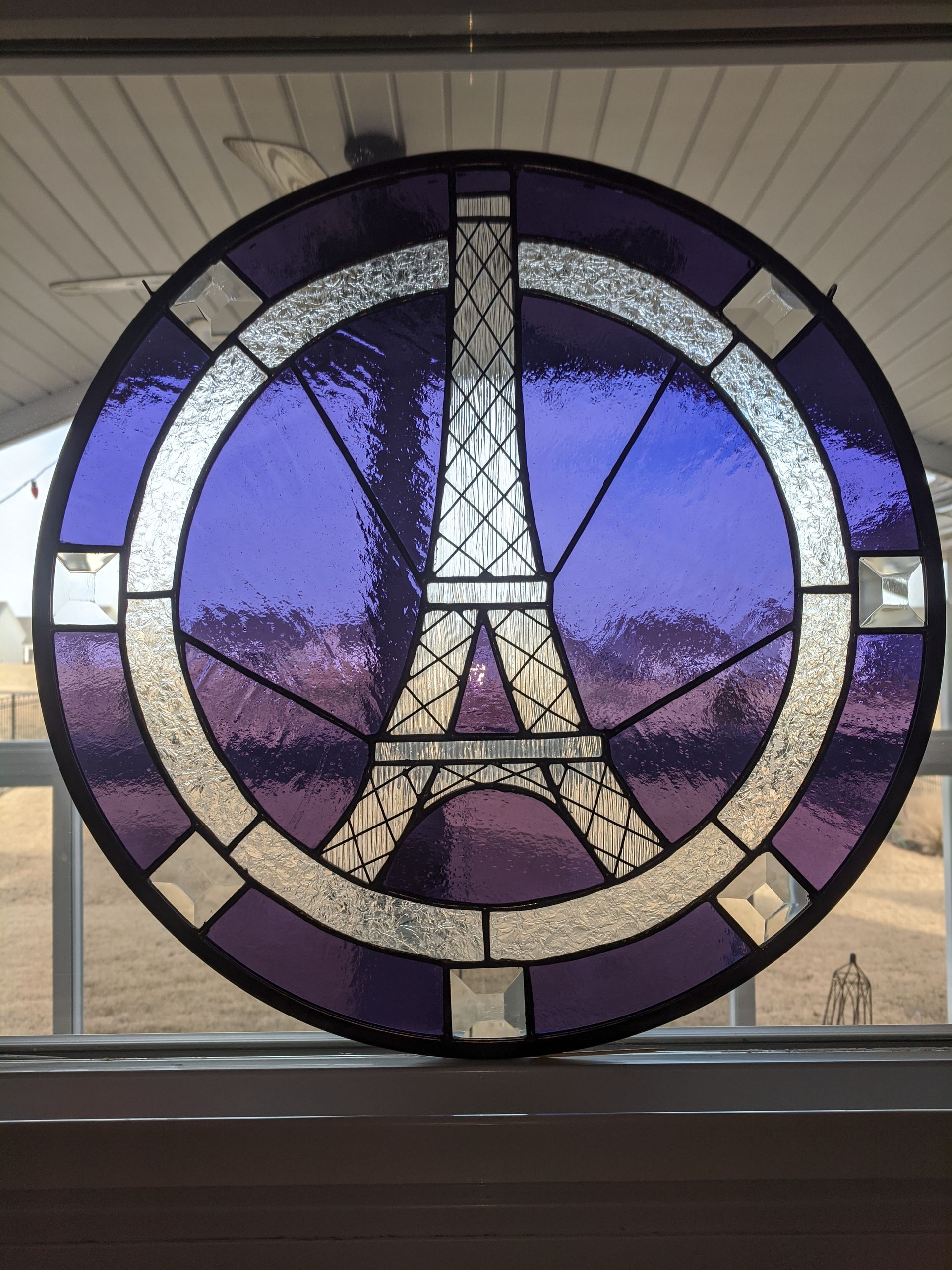 Circular stained-glass window with the Eiffel Tower in purple, white, and gold tones