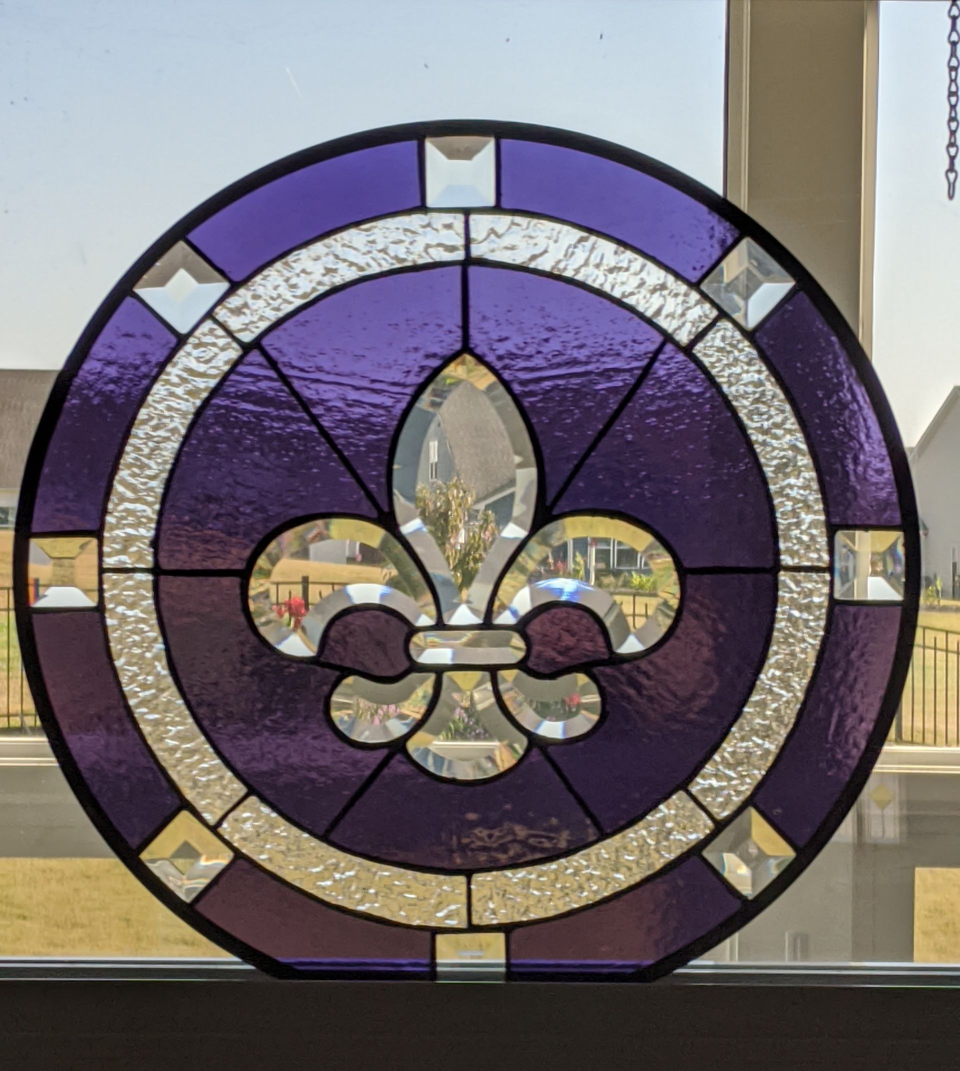 Purple stained-glass circular window with a central fleur-de-lis and white mosaic border