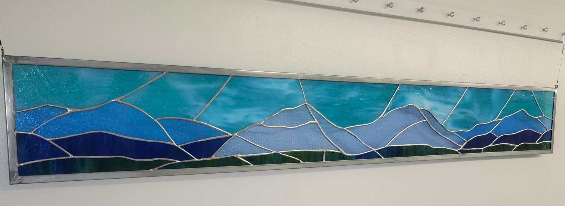 Colorful abstract glass wall art with blue, green, and white geometric mountain-like shapes