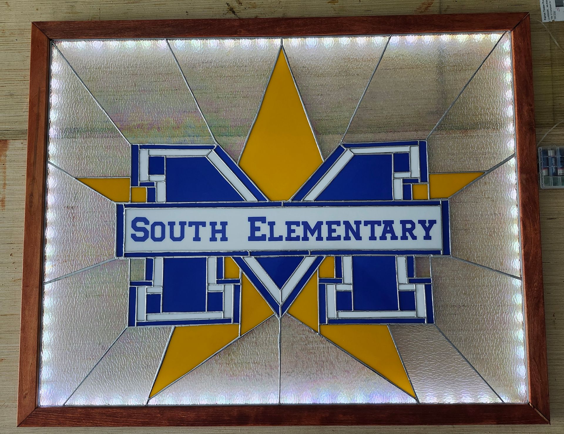 South Elementary school logo on a blue and yellow star mosaic with a wooden frame