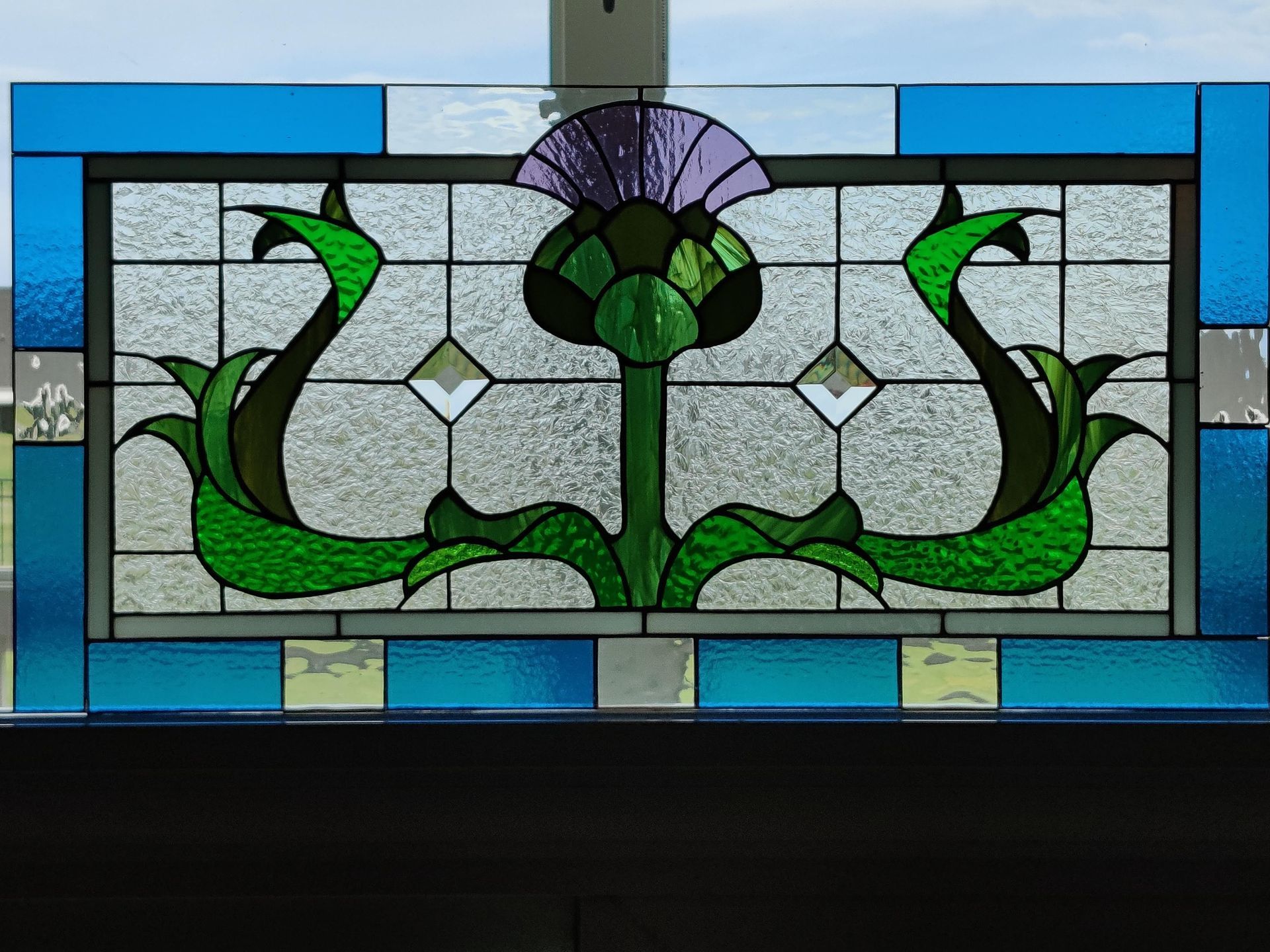 Stained glass panel with green vines, purple flower, and blue border on a window.