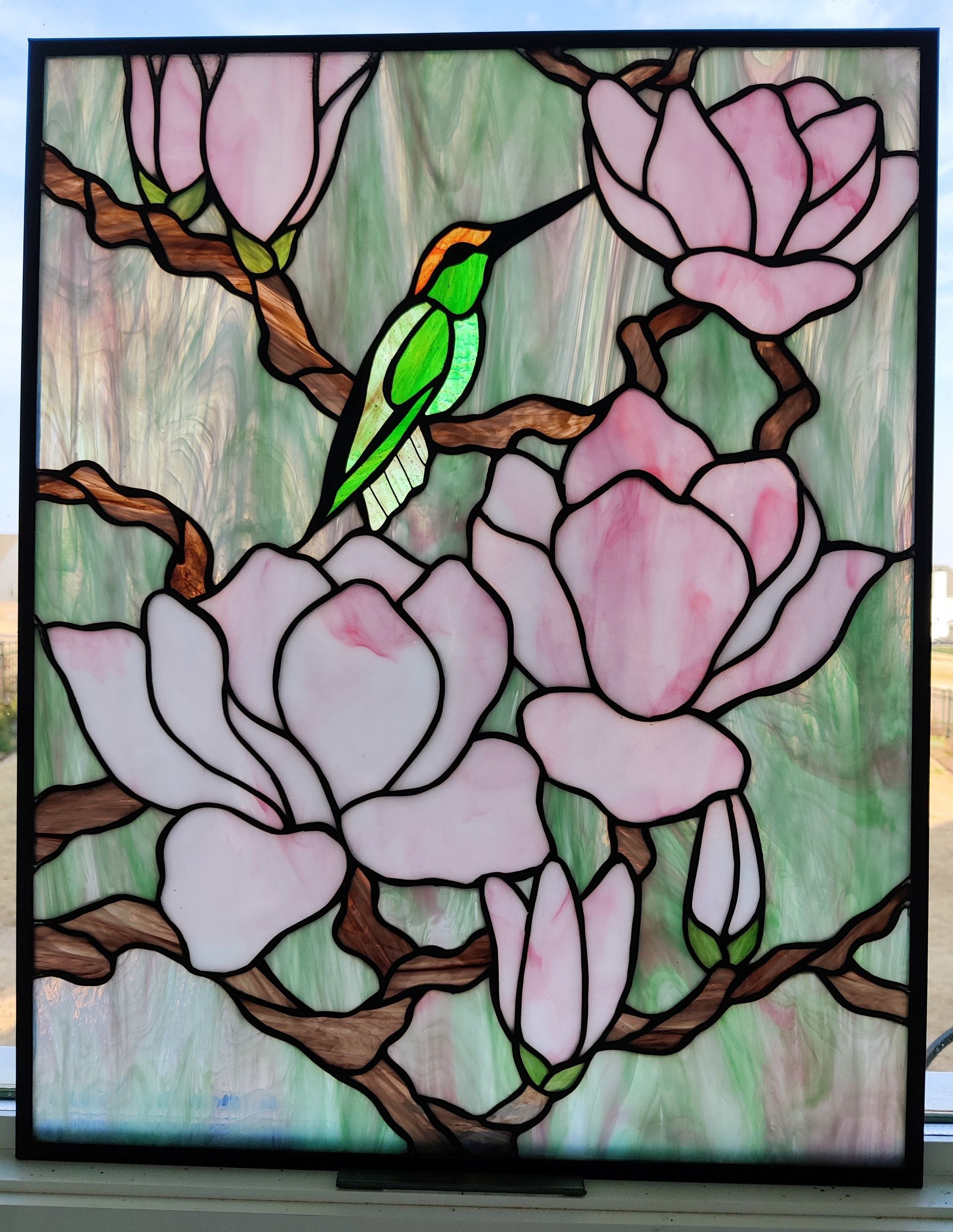 Stained-glass style floral scene with pink magnolias, brown branches, and a green bird on a branch.