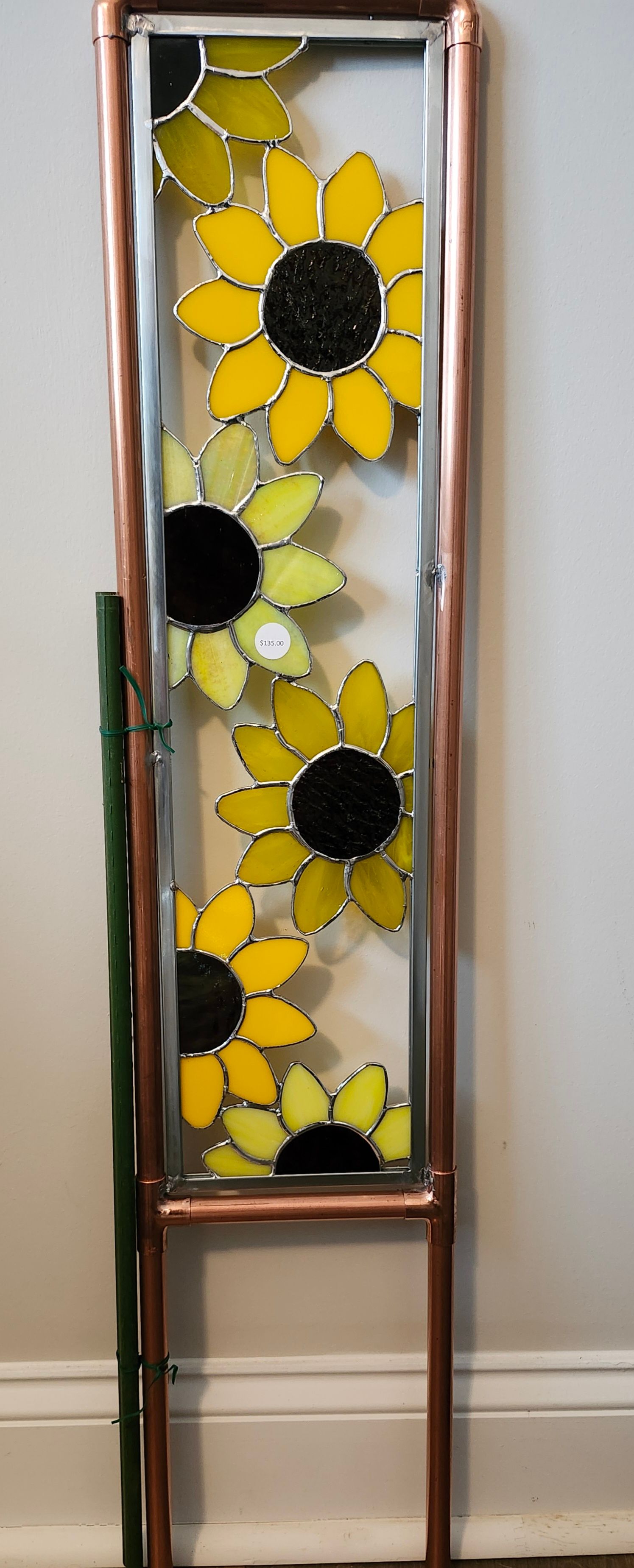 Tall narrow stained-glass panel with yellow sunflowers and a copper frame on a stand