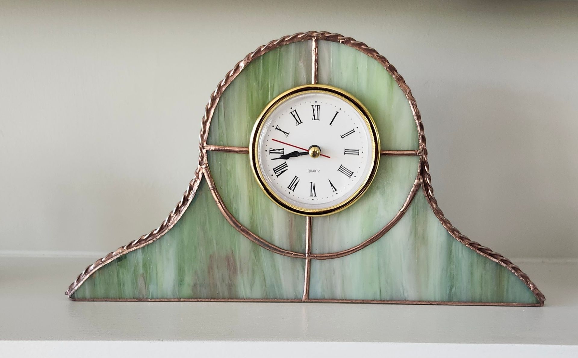 Decorative wall clock with a white face on a green and copper arched frame