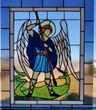 Stained-glass angel with wings, sword, and blue robe standing over a green dragon-like figure.