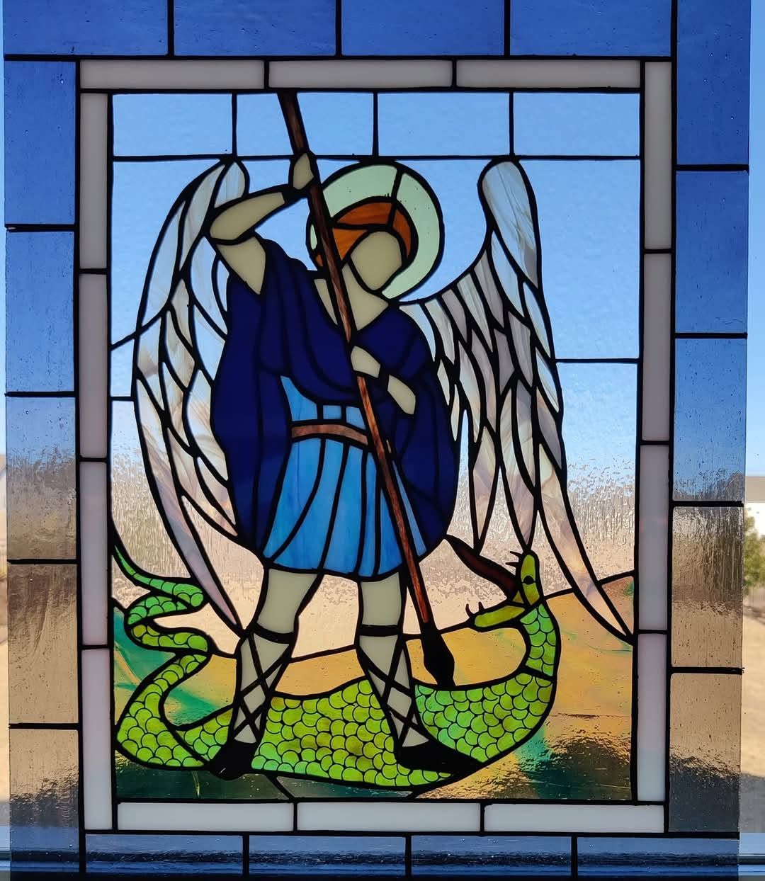 Stained-glass angel with wings, sword, and blue robe standing over a green dragon-like figure.