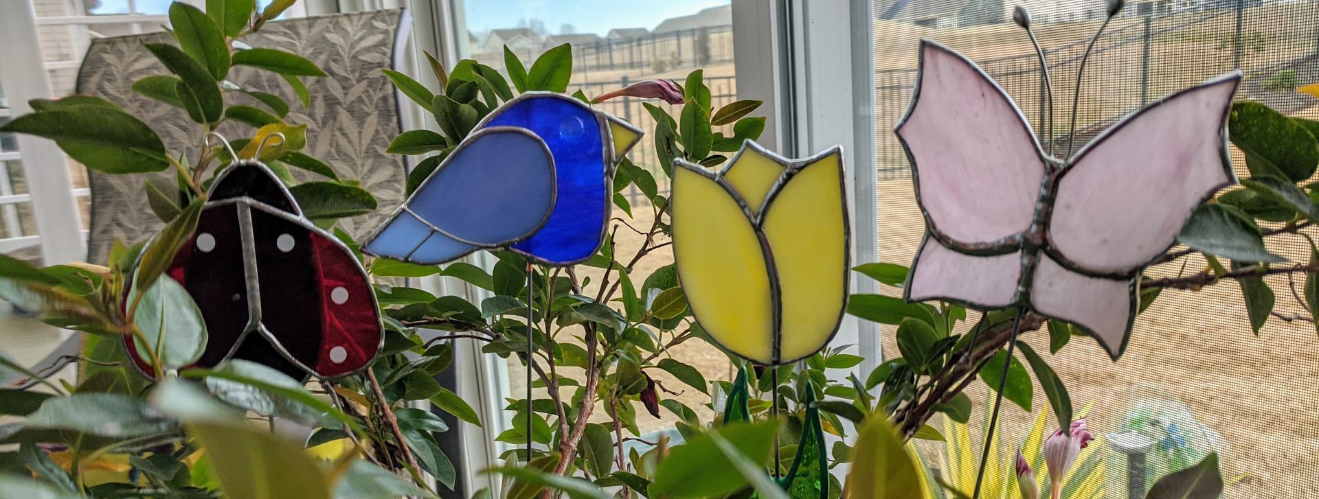 Colorful butterfly garden sculpture with a blue, yellow, and pink butterfly against a fence