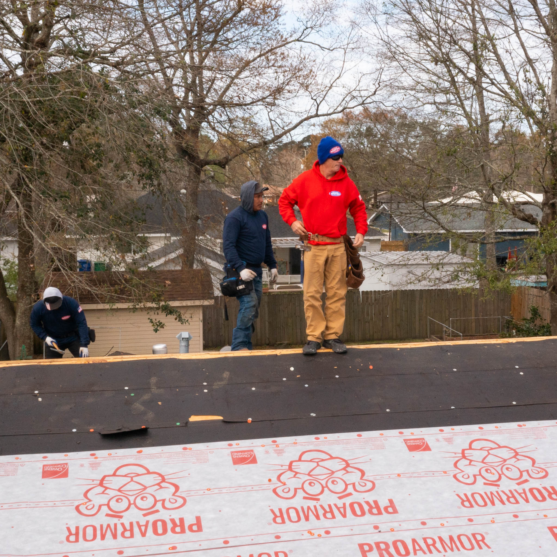 A man in a red shirt is standing on a roof with proarmor laying on it