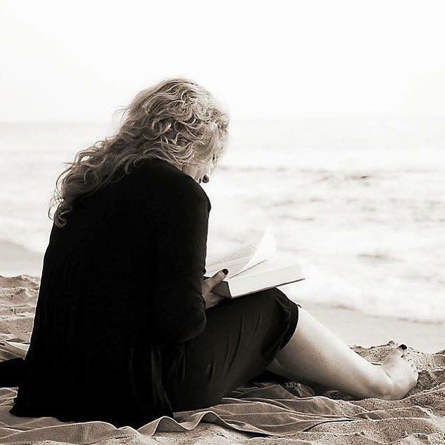 Una persona seduta su una spiaggia sabbiosa legge un libro in riva all'oceano.