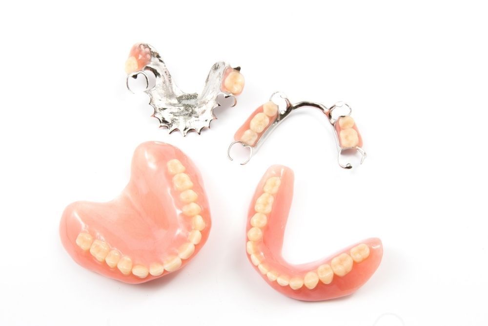 Dentures: Full upper and lower sets, plus two partial dentures with metal framework, on white.