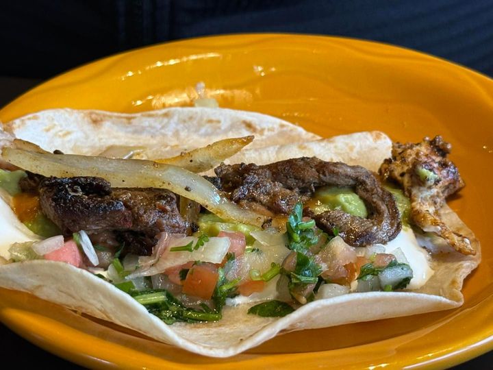 A steak taco with grilled onions, salsa, and cilantro on a soft flour tortilla, served on a round yellow plate.