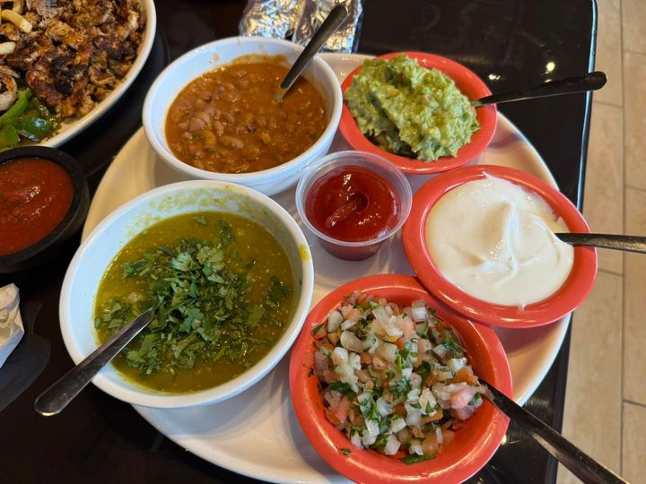 A platter with bowls of pinto beans, guacamole, sour cream, pico de gallo, green salsa, and a small cup of red salsa.