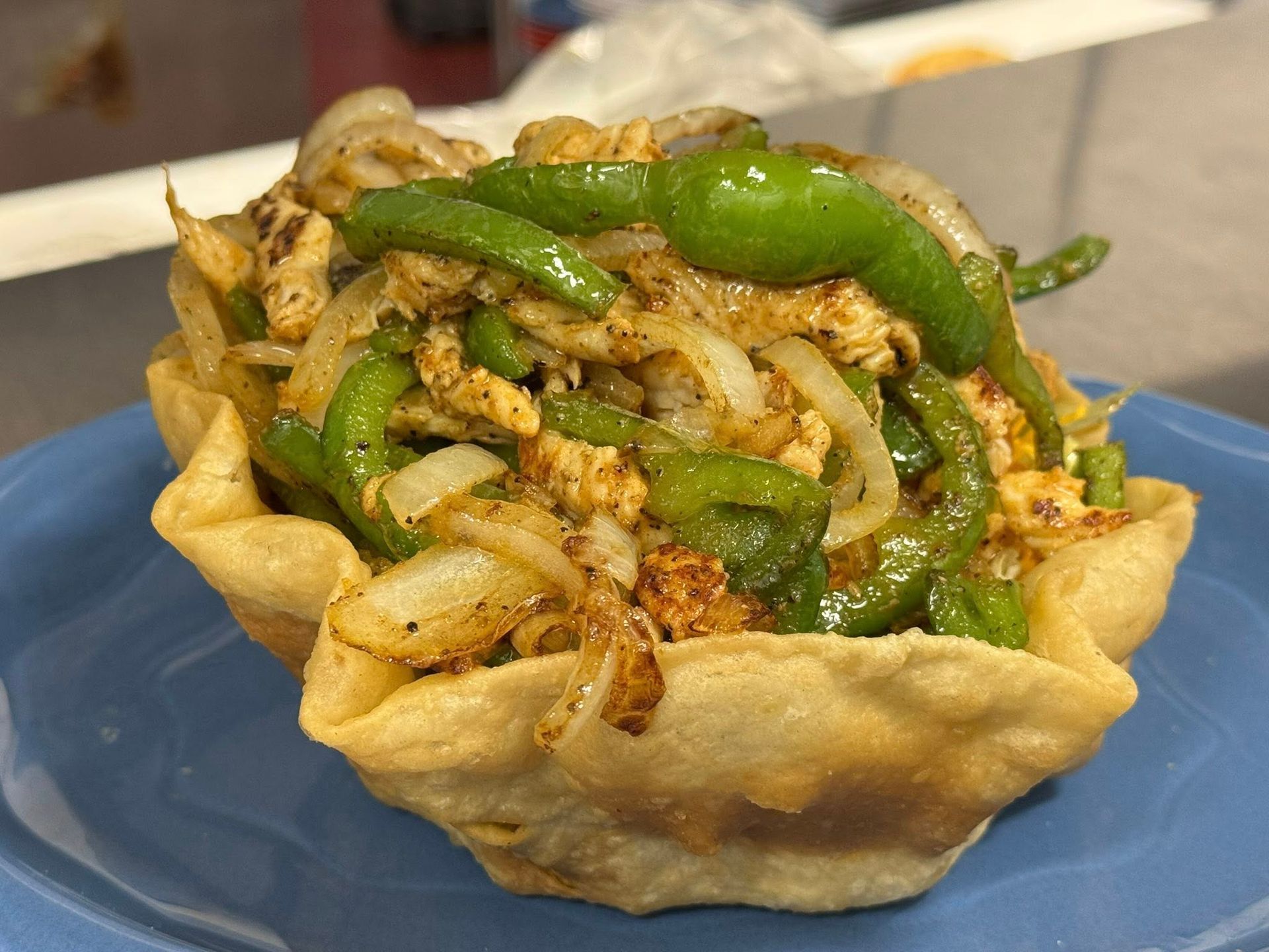 Sautéed chicken, onions, and green peppers served in a crispy, golden fried tortilla bowl on a blue plate.