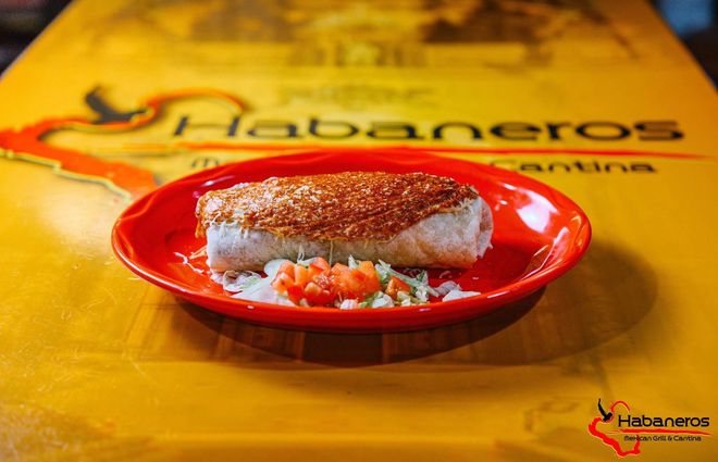 A burrito topped with melted cheese and red sauce on a red plate, set on a yellow Habaneros restaurant table.