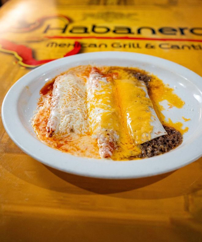 A plate of three enchiladas with different sauces and melted cheeses on a restaurant table at Habanero Mexican Grill.