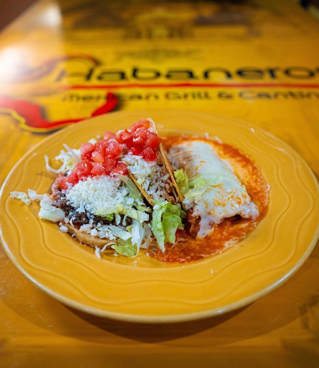 A taco and an enchilada topped with lettuce, cheese, and tomatoes on a yellow plate at Habaneros restaurant.