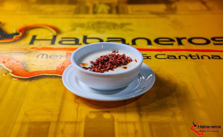 A white bowl of creamy soup topped with reddish garnish, served on a saucer atop a yellow Habaneros restaurant table.