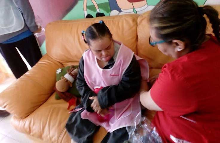Una mujer con un delantal rosa está sentada en un sofá con otra mujer.
