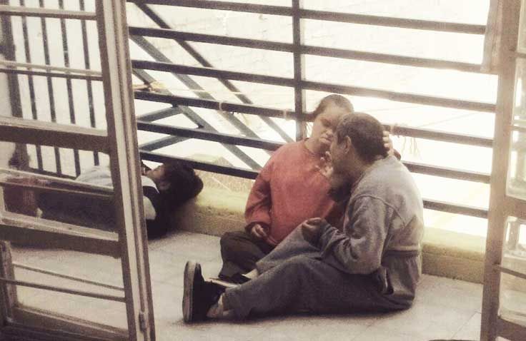Dos personas están sentadas en el suelo delante de una valla.