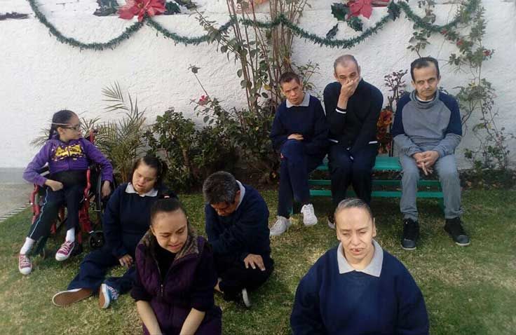 Un grupo de personas está sentada en el césped frente a una pared blanca.