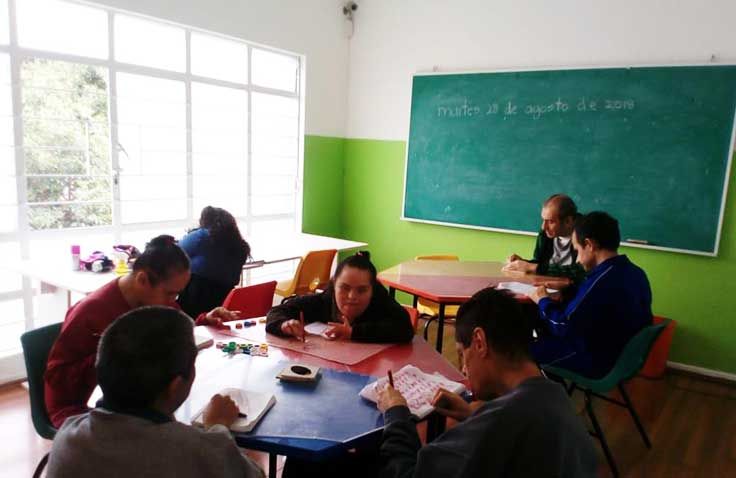 Un grupo de personas está sentado alrededor de una mesa frente a una pizarra verde.