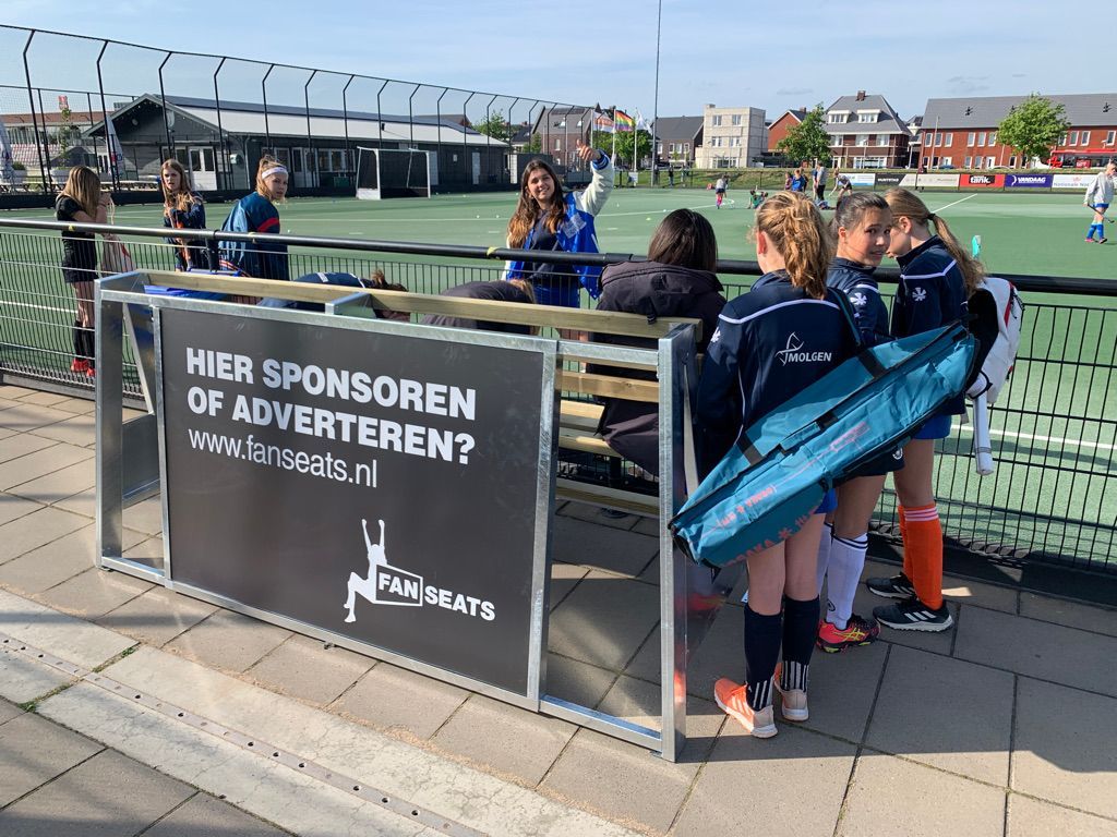 Hockeyspelers staan ​​bij een bankje met een reclamebord waarop staat: 