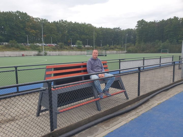 Een man zit op het prototype van de eerste Fanseats bank met uitzicht op een hockeyveld.